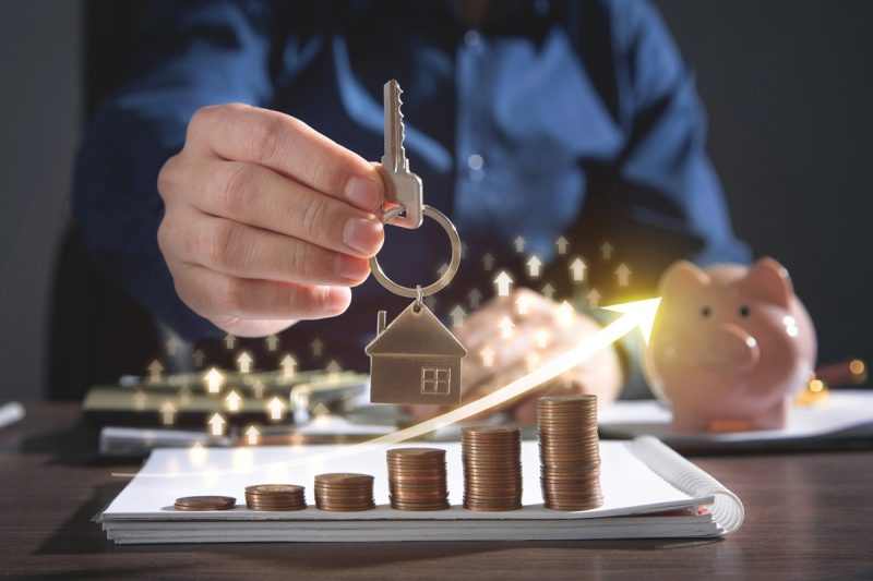 Real estate agent showing house key over stack of coins. Real Estate Graph. House market growth